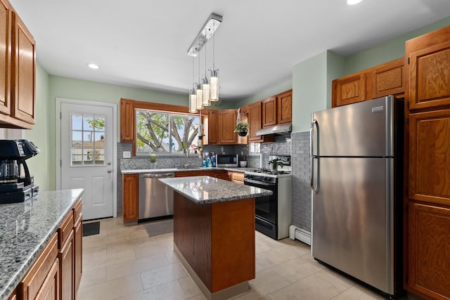 kitchen featuring appliances with stainless steel finishes, under cabinet range hood, light stone counters, backsplash, and a baseboard radiator