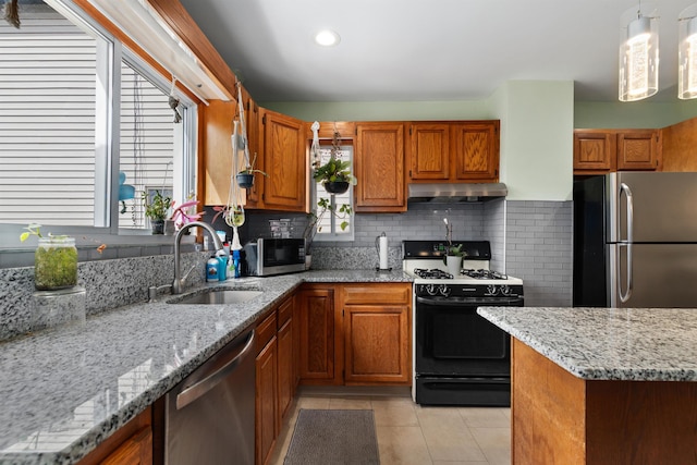 kitchen with appliances with stainless steel finishes, a sink, under cabinet range hood, brown cabinets, and light tile patterned floors