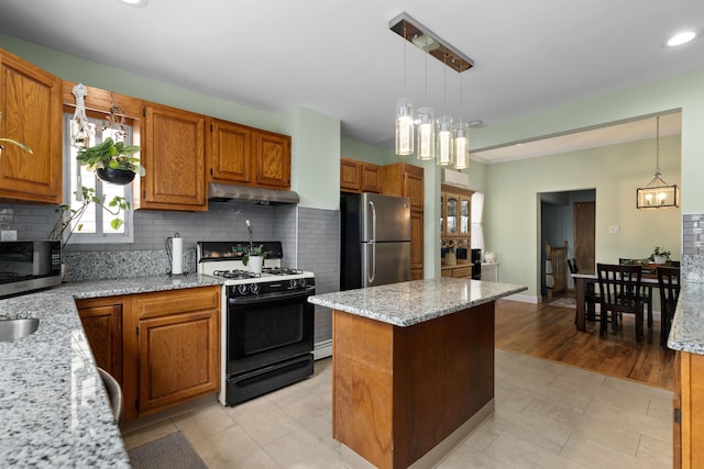 kitchen with appliances with stainless steel finishes, under cabinet range hood, decorative backsplash, a kitchen island, and recessed lighting