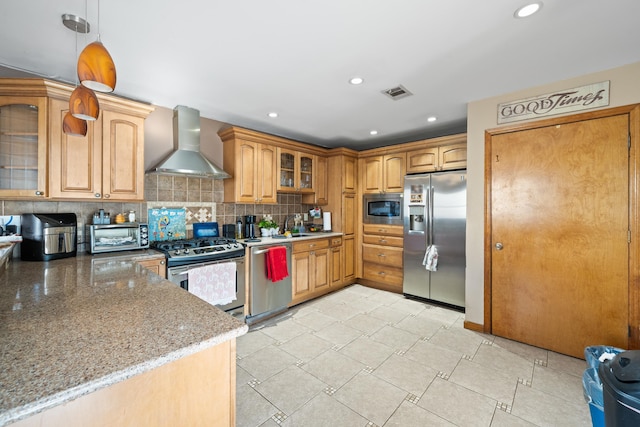 kitchen with stainless steel appliances, wall chimney range hood, light stone counters, backsplash, and decorative light fixtures