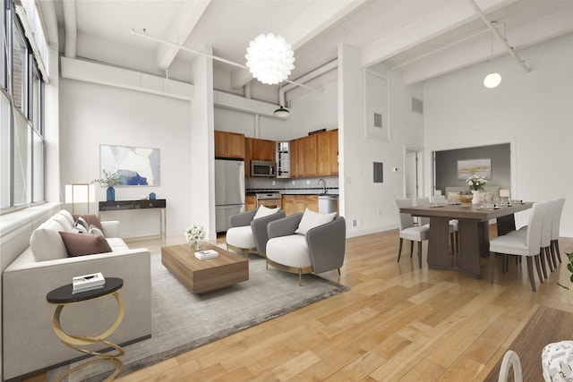 living room featuring a towering ceiling, light wood-style floors, beamed ceiling, baseboards, and a chandelier