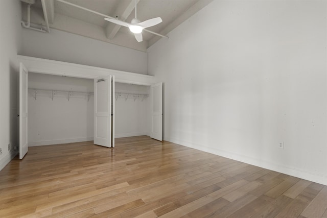 unfurnished bedroom featuring multiple closets, light wood-style flooring, high vaulted ceiling, a ceiling fan, and baseboards