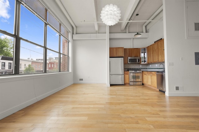kitchen featuring appliances with stainless steel finishes, a sink, brown cabinetry, backsplash, and light wood-style floors