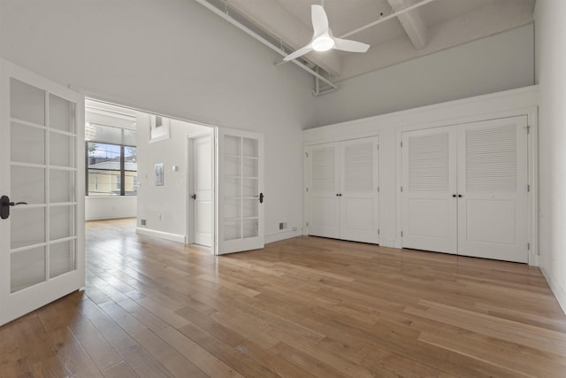 unfurnished bedroom featuring french doors, a towering ceiling, two closets, wood finished floors, and a ceiling fan