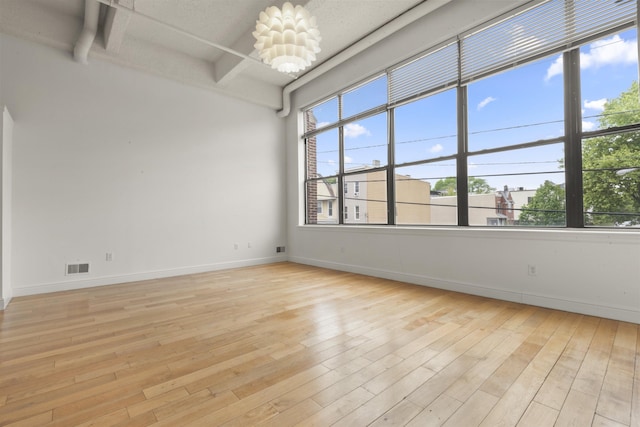 empty room with light wood-style flooring, baseboards, beam ceiling, and a chandelier