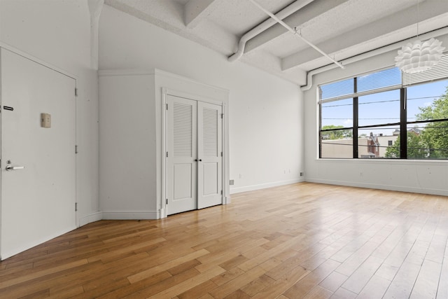 empty room featuring light wood-style floors, beam ceiling, and baseboards
