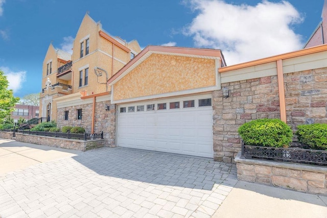 view of front facade featuring decorative driveway, a garage, stone siding, and stucco siding