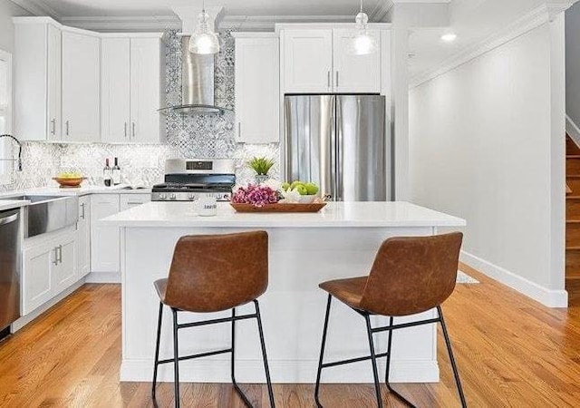 41 Graham St Unit 2, Jersey City, NJ 07307 - kitchen with appliances with stainless steel finishes, wall chimney range hood, a sink, a breakfast bar, and ornamental molding