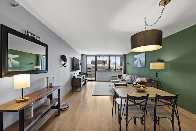 dining space with a baseboard radiator, expansive windows, baseboards, and light wood finished floors