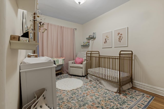 bedroom featuring baseboards, a crib, and wood finished floors