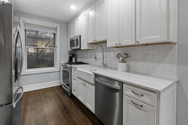kitchen with a sink, stainless steel appliances, white cabinetry, baseboards, and dark wood-style floors