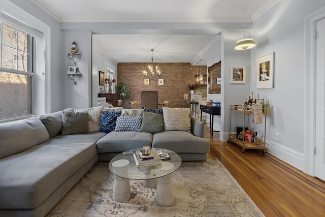 living room featuring baseboards, brick wall, a chandelier, crown molding, and wood finished floors