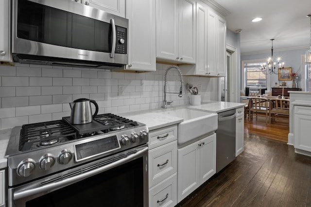 kitchen with a sink, white cabinets, dark wood-style flooring, appliances with stainless steel finishes, and a chandelier