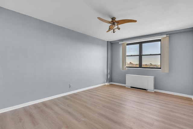 spare room featuring light wood-type flooring, radiator, and ceiling fan