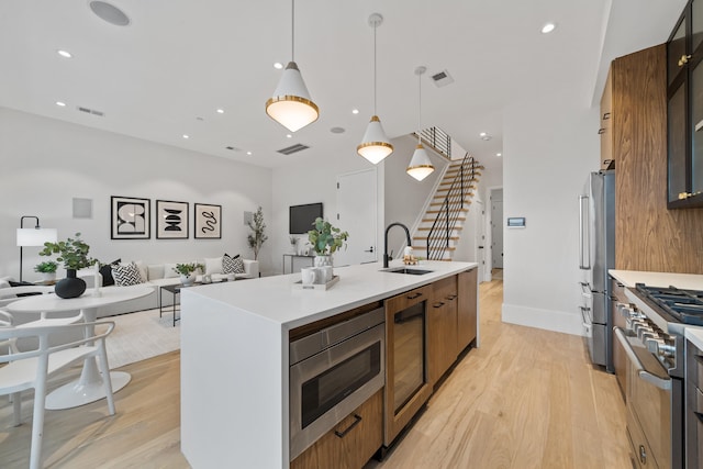 kitchen featuring wine cooler, appliances with stainless steel finishes, decorative light fixtures, light wood-type flooring, and a center island with sink