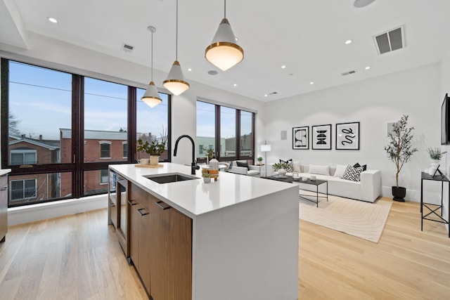 kitchen featuring decorative light fixtures, a kitchen island with sink, light hardwood / wood-style floors, and sink