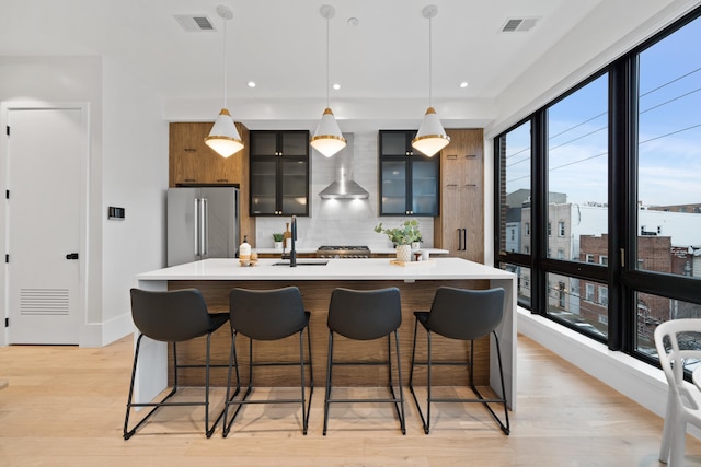 kitchen with a kitchen breakfast bar, hanging light fixtures, wall chimney range hood, an island with sink, and high end refrigerator