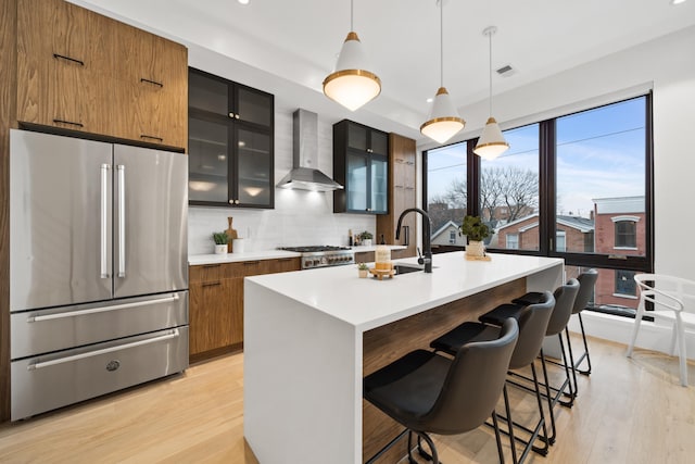 kitchen featuring hanging light fixtures, wall chimney exhaust hood, plenty of natural light, an island with sink, and stainless steel refrigerator