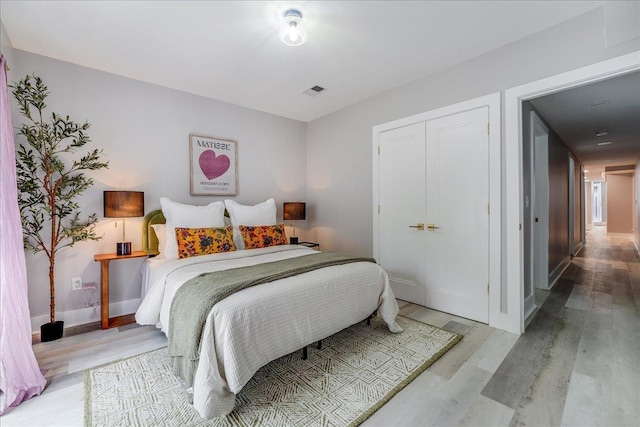 bedroom featuring light wood-style flooring, baseboards, visible vents, and a closet