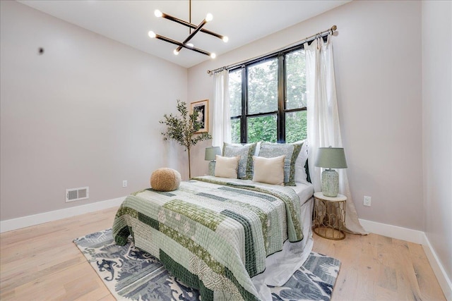 bedroom with a notable chandelier, wood finished floors, visible vents, and baseboards