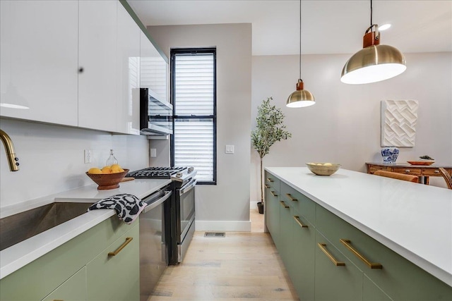 kitchen featuring light wood-style flooring, a sink, appliances with stainless steel finishes, green cabinets, and light countertops