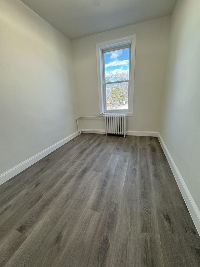 spare room with dark wood-type flooring, radiator, and baseboards