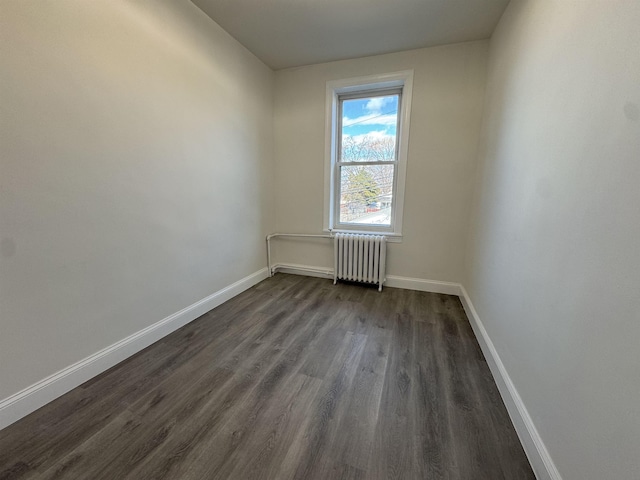 empty room with dark wood-style floors, radiator, and baseboards