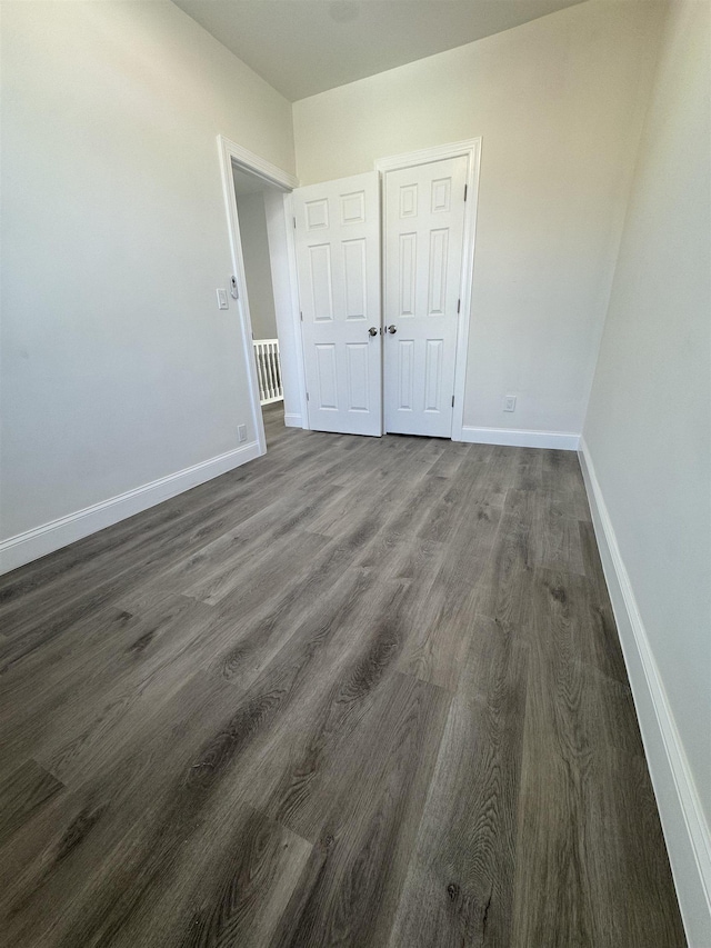 unfurnished bedroom featuring a closet, baseboards, and dark wood-style flooring