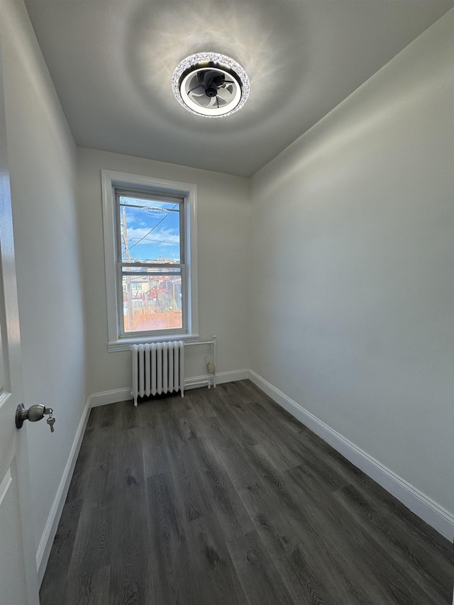 spare room featuring radiator, baseboards, and dark wood-type flooring