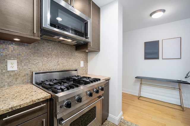 kitchen featuring dark brown cabinets, stainless steel appliances, light stone counters, light hardwood / wood-style floors, and decorative backsplash