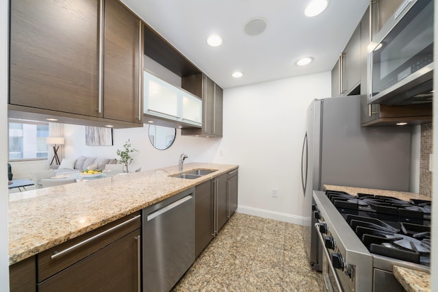 kitchen with dark brown cabinetry, sink, light stone countertops, and appliances with stainless steel finishes