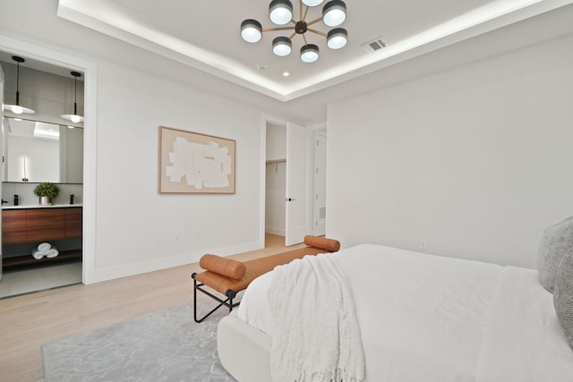 bedroom with hardwood / wood-style flooring, a walk in closet, an inviting chandelier, and a tray ceiling