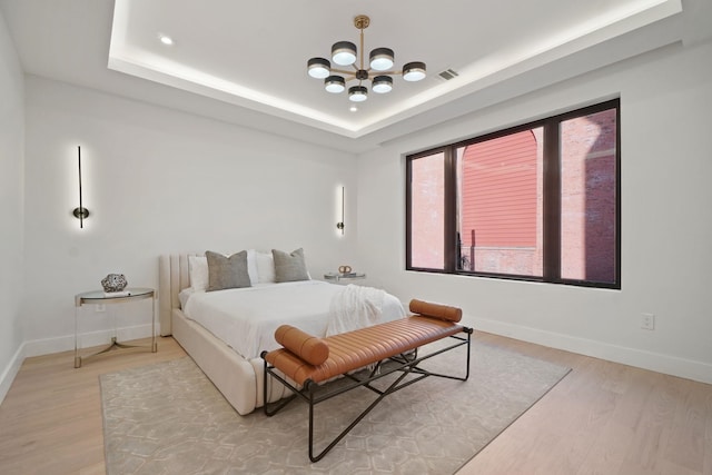 bedroom with a tray ceiling, a chandelier, and light hardwood / wood-style floors