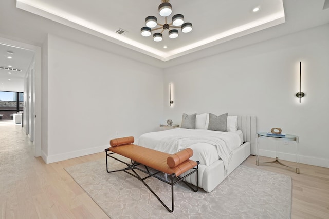 bedroom with a raised ceiling, an inviting chandelier, and light wood-type flooring