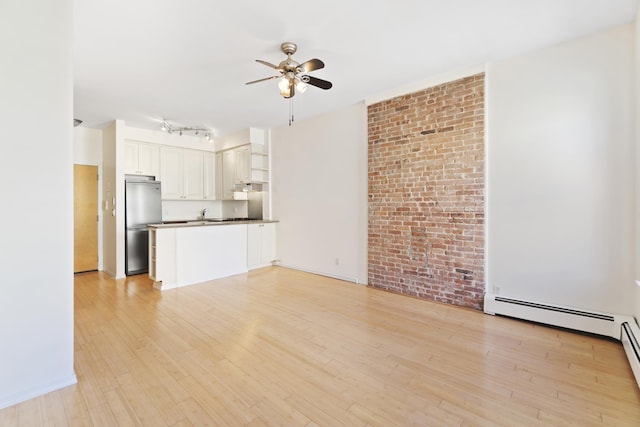 unfurnished living room with a ceiling fan, a baseboard radiator, brick wall, rail lighting, and light wood-style floors