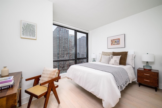 bedroom with expansive windows, baseboards, and wood finished floors