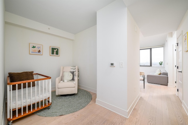 bedroom featuring baseboards, a crib, and wood finished floors