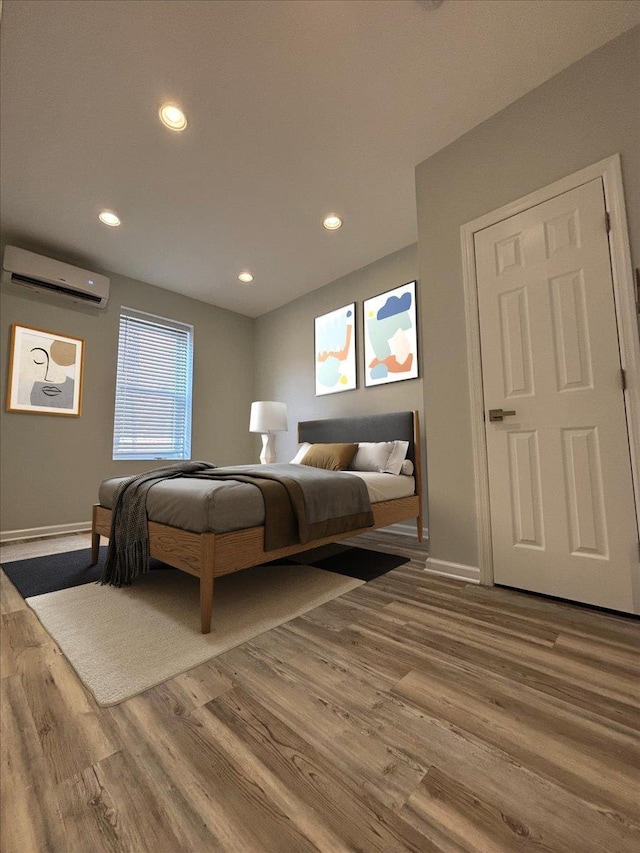 bedroom featuring baseboards, recessed lighting, wood finished floors, and a wall unit AC