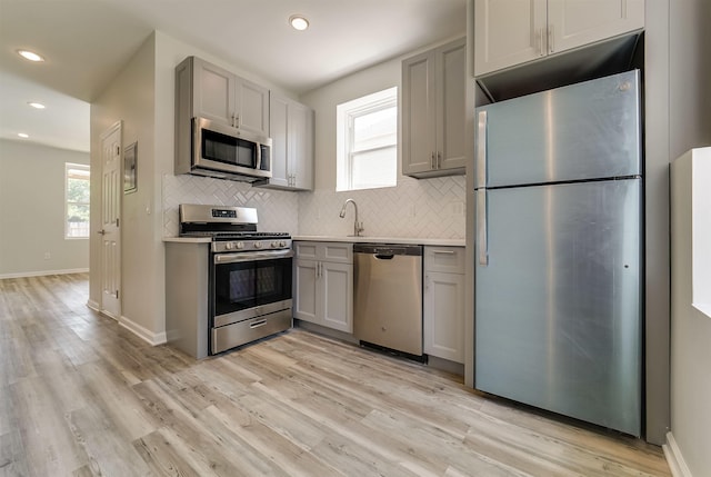 kitchen with light wood-style flooring, recessed lighting, appliances with stainless steel finishes, gray cabinetry, and backsplash