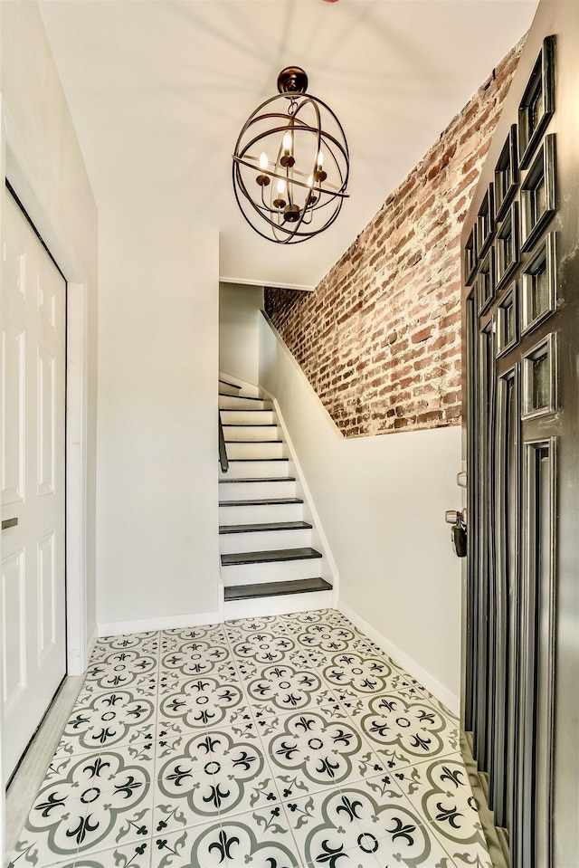 foyer entrance featuring a chandelier, stairs, brick wall, and baseboards