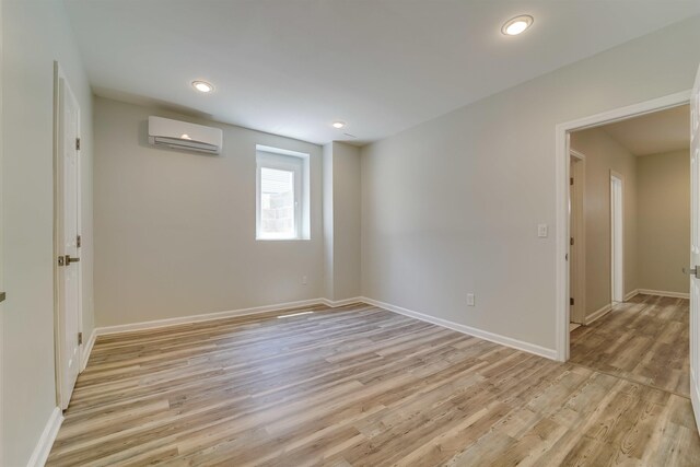 empty room with baseboards, light wood finished floors, recessed lighting, and a wall unit AC