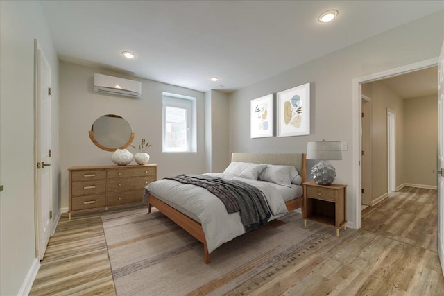bedroom featuring a wall unit AC, light wood finished floors, baseboards, and recessed lighting