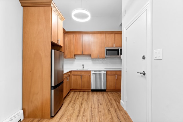 kitchen featuring decorative backsplash, stainless steel appliances, sink, a baseboard radiator, and light hardwood / wood-style floors