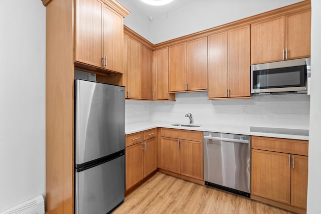 kitchen featuring appliances with stainless steel finishes, light wood-type flooring, backsplash, a baseboard heating unit, and sink