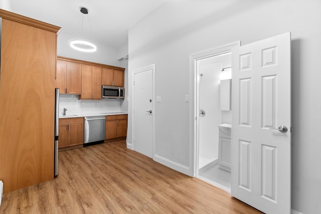 kitchen featuring sink, hanging light fixtures, stainless steel appliances, light hardwood / wood-style flooring, and decorative backsplash