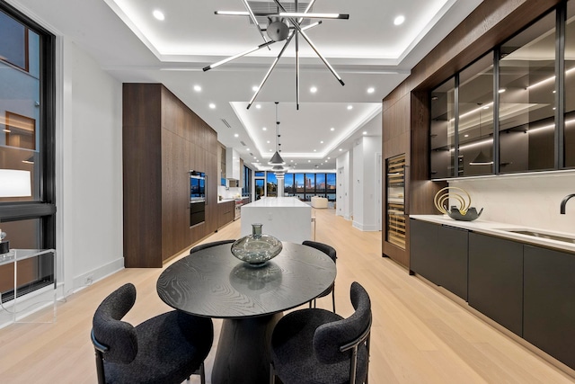 dining area with a tray ceiling, sink, and light hardwood / wood-style floors