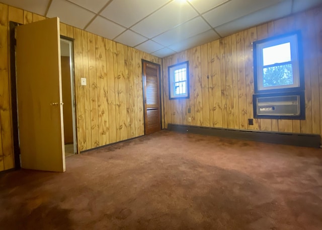 carpeted empty room featuring a paneled ceiling, a wall mounted air conditioner, and wooden walls