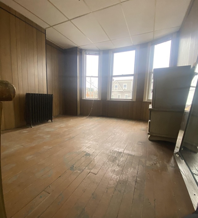 spare room with hardwood / wood-style flooring, radiator heating unit, a paneled ceiling, and wood walls