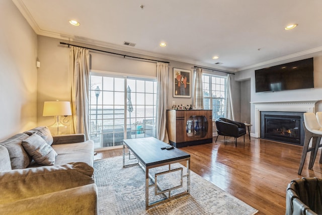 living room with a glass covered fireplace, wood finished floors, visible vents, and ornamental molding