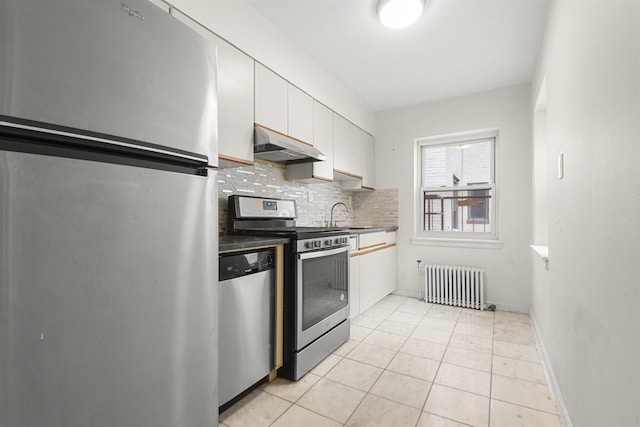 kitchen with tasteful backsplash, under cabinet range hood, radiator heating unit, white cabinets, and stainless steel appliances